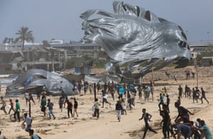 People run towards two large grey parachutes with the ruins of a building behind them