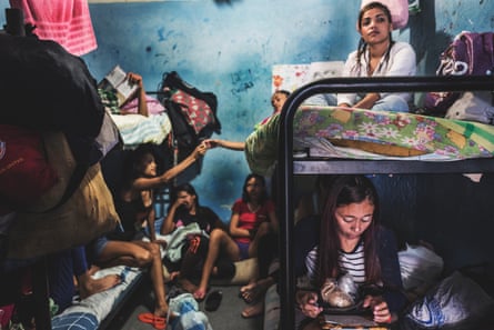 Women sit on two bunkbeds and on the floor of an overcrowded prison cell.