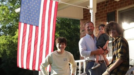 A man on a porch with an American flag behind him. There are three boys of different ages in the foreground