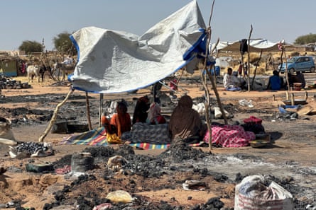 Displaced Sudanese people who left El Fasher after its fall, sit in the shade in Tawila amid the remains of a fire that broke out in the camp on 11 February.