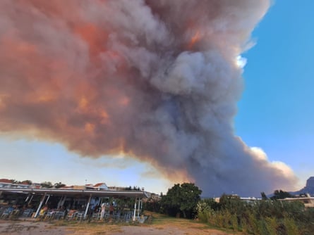 Plumes of smoke billow in the distance in Rhodes, with buildings in the foreground