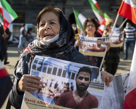 A woman holds a poster with a picture of a man. Other people can be seen holding flags behind her