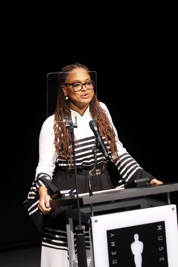 A woman with long braids speaks at a podium on stage.