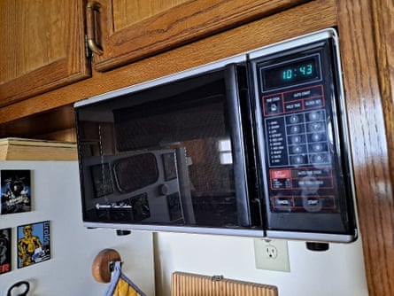 A black wall-mounted microwave sits below wooden kitchen cupboards