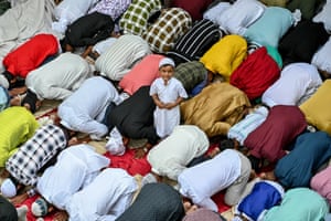 A child looks up at the camera as Muslim devotees kneel in prayer
