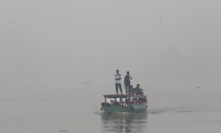 Students ride on a boat while haze from wildfires blanket the Musi River in Palembang, Indonesia