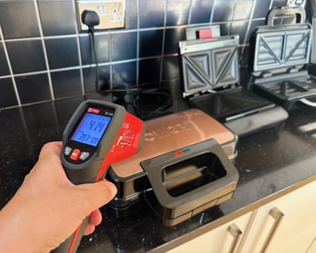 A hand comes into bottom right of frame with a digital thermometer over a closed toastie maker.