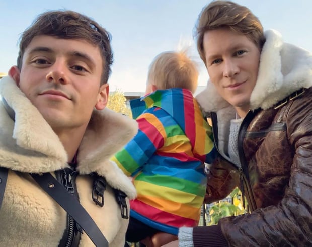Tom Daley with his husband, Dustin Lance Black, and their son, Robbie, wearing a rainbow coat