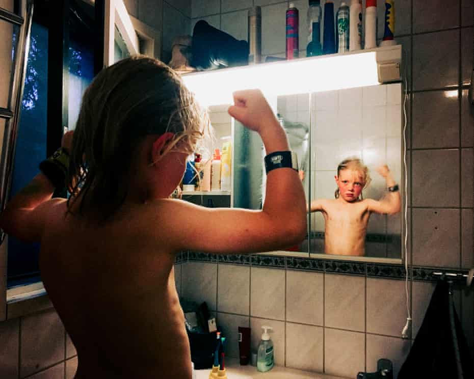 Photograph of young boy flexing his arm muscles in a bathroom mirror