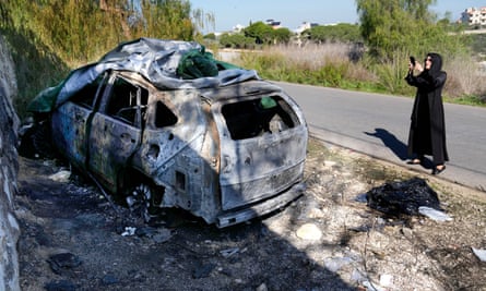 Une femme photographie la voiture incendiée avec son téléphone portable