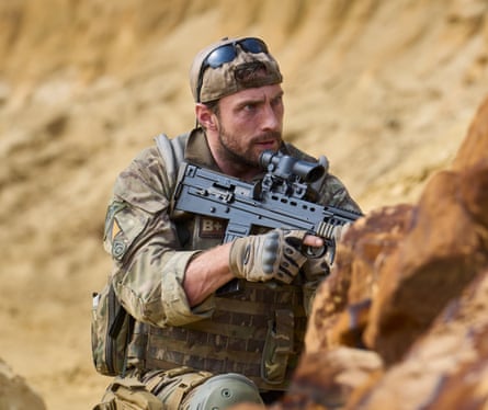 A man in army fatigues hiding behind a rock holding a machinegun