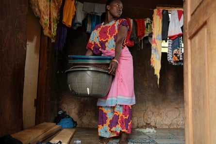 A woman in a colourful dress stands alongside washing that has been hung out to dry, holding a stack of plastic buckets