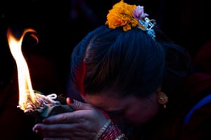A woman with a magnolia in her hair bows her head and raises hands holding a burning offering to her forehead