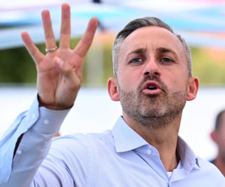 Man with stubble and short hair wearing a blue shirt holding up four fingers.