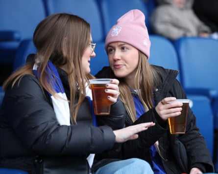 Two Chelsea fans, each with a pint of beer in hand, are deep in discussion during their team's Women's Super League game at home against West Ham at Kingsmeadow.