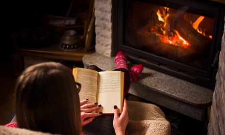 Woman reads a book by the fireplace.