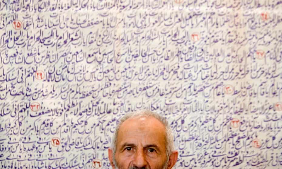 An Iranian man sits in front of holy scroll.