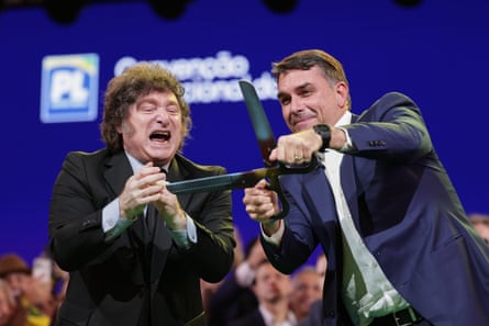 Flávio Bolsonaro wields a pair of hedge trimmer shears and pretends to cut something as Milei applauds