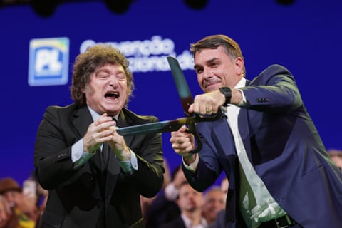 Flávio Bolsonaro wields a pair of hedge trimmer shears and pretends to cut something as Milei applauds