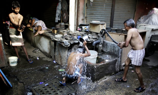 Indian migrant daily wage workers bath at a public well
