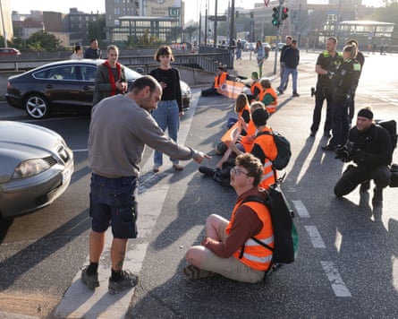 A man pointing angrily at a protesters sitting on the ground alongside other protesters.