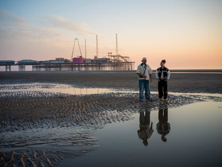 Two young people standing on the beach at sunset with Blackpool’s South Pier in the background.
