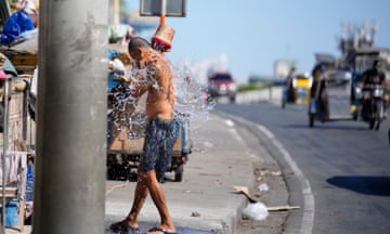 A man wearing only shorts pours water over himself at the side of a road