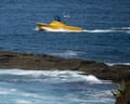 A yellow boat cutting through ocean water near a beach.