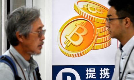 Tokyoites walk past a Bitcoin currency poster at the entrance of an electronics store.