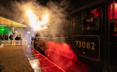 A steam train pulls into a platform where people are waiting at night.