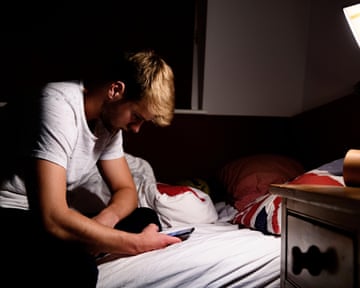 Young man looks at his phone in his bedroom at night