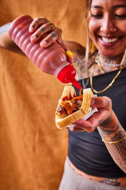 A woman pouring tomato sauce on to a sausage sizzle sandwich.