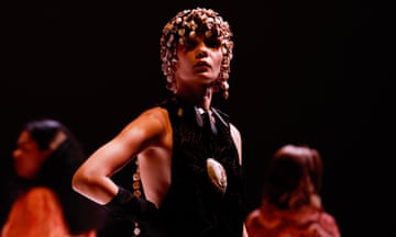A model wears a shell headpiece and a black dress at a fashion show.