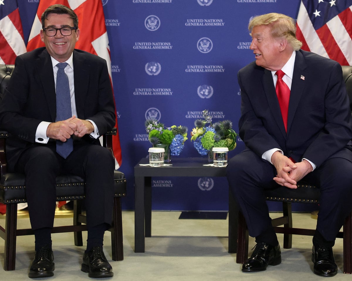 Two men in suits sitting on chairs with a UK and US flag visible in the background.