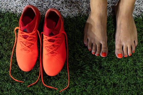 A pair of orange football boots next to a woman’s feet