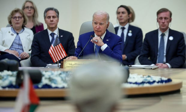 Joe Biden sits at a large round table with an American flag at his elbow.