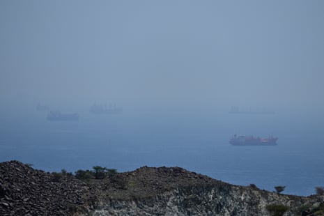 Tankers and bulk carriers sit in the strait of Hormuz, hazy and blue-grey in a fog.