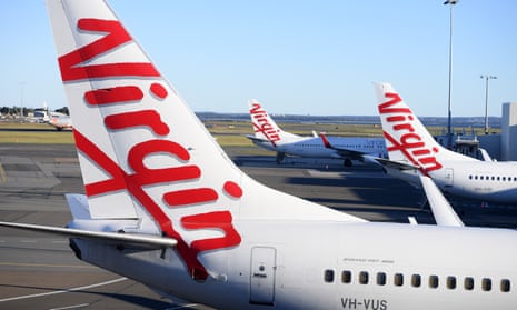 The tails of three Virgin Australia planes lined up at an airport terminal