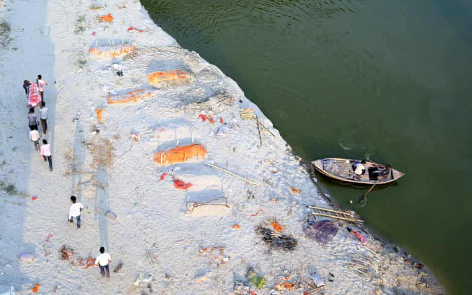 Family members and relatives carry a body past burial sites on the banks of river.