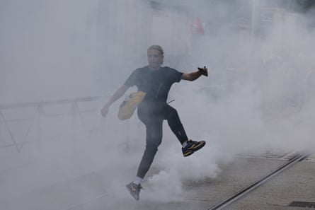 A student kicks a tear gas canister on a street shrouded in smoke and gas.