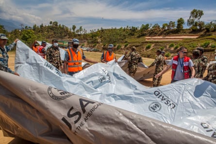 A group of people hold a large grey tarpaulin with the letters ‘USAID’ on it