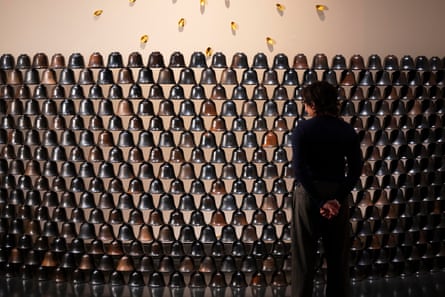 A silhouetted figure stands in front of a wall of terracotta bells
