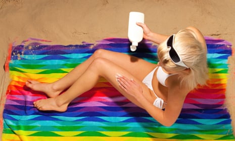 Overhead shot of a woman in a white bikini sitting on a beach towel applying suntan cream.BGM5JB Overhead shot of a woman in a white bikini sitting on a beach towel applying suntan cream.