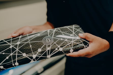A Rolls-Royce craftsperson holds a carbon-fibre panel etched with a bitcoin symbol