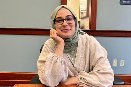 person wearing glasses, light green head covering and ivory top sits at table