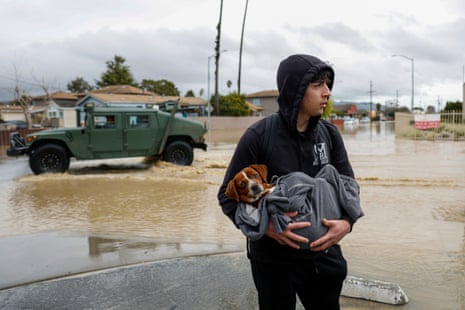 A young man holds his dog on the flooded streets of Pajaro, California.