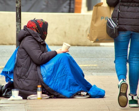 A homeless person begs in the street with her faced turned away from the camera