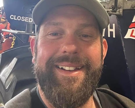 James Desborough: in this closeup image he wears a peaked cap and is smiling. He has a brown beard.