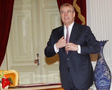 Prince Andrew in 2011: he is walking through a room with a white wooden panelled doorway and red velvet curtains, with a blue-patterned vase behind him. He wears a dark suit.