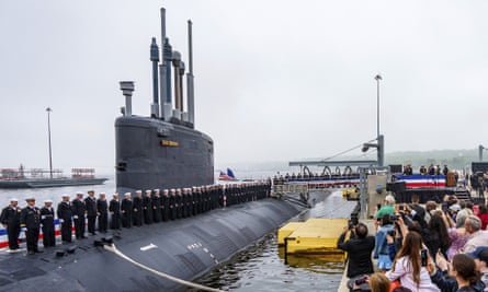 Sailors stand at attention on the deck of a submarine alongside a pier